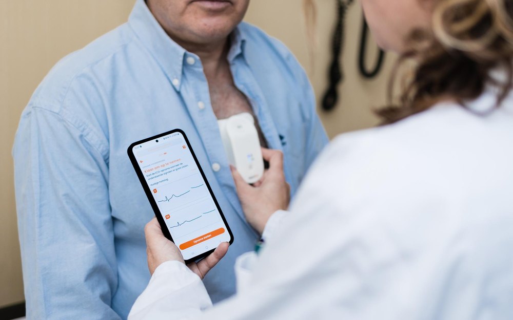 A clinician viewing a 12-lead ECG on a smartphone while a pocket-sized HeartEye ECG device rests on a patient’s chest.