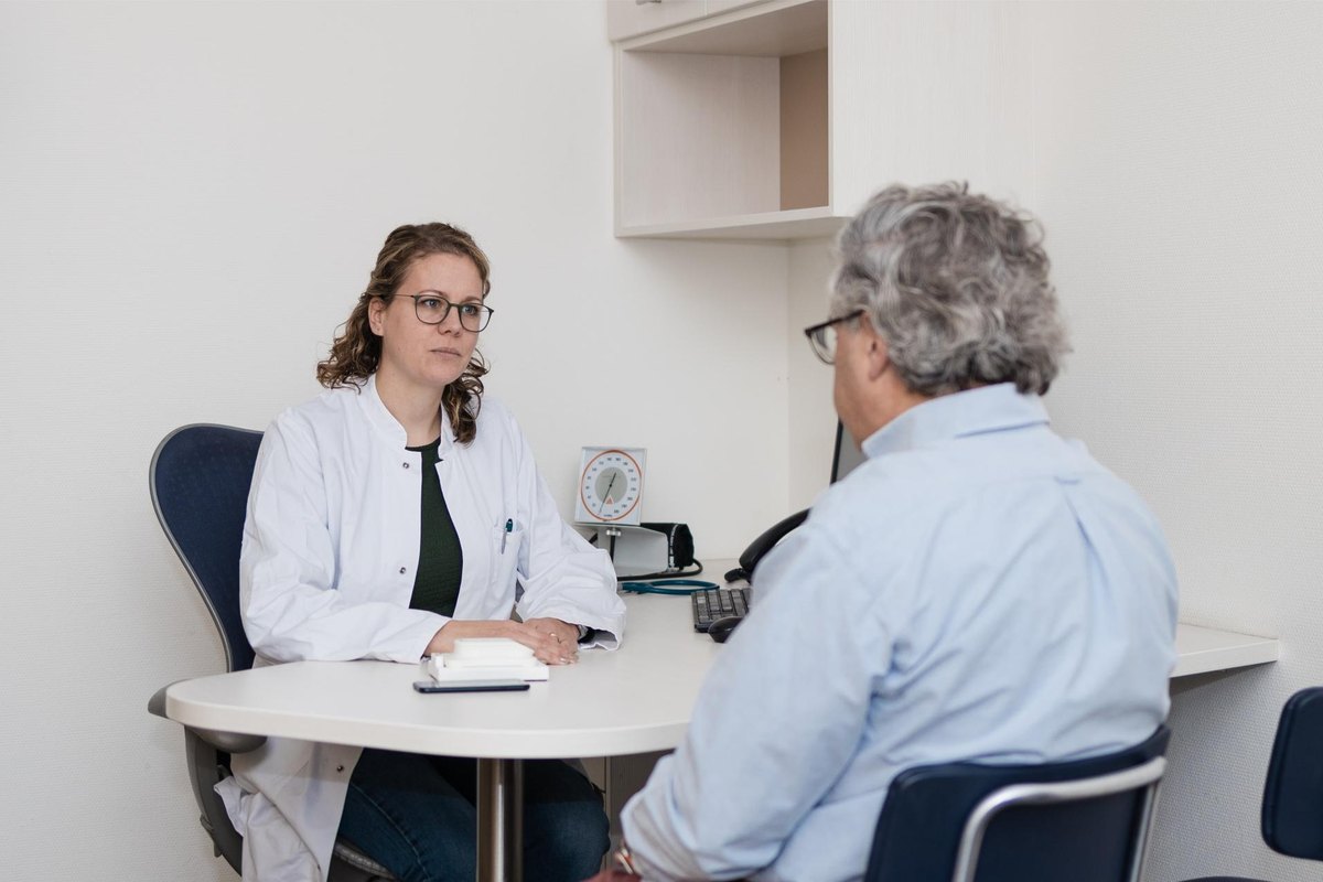 A clinician and a patient seated at a consultation table, with the HeartEye ECG device on the table.