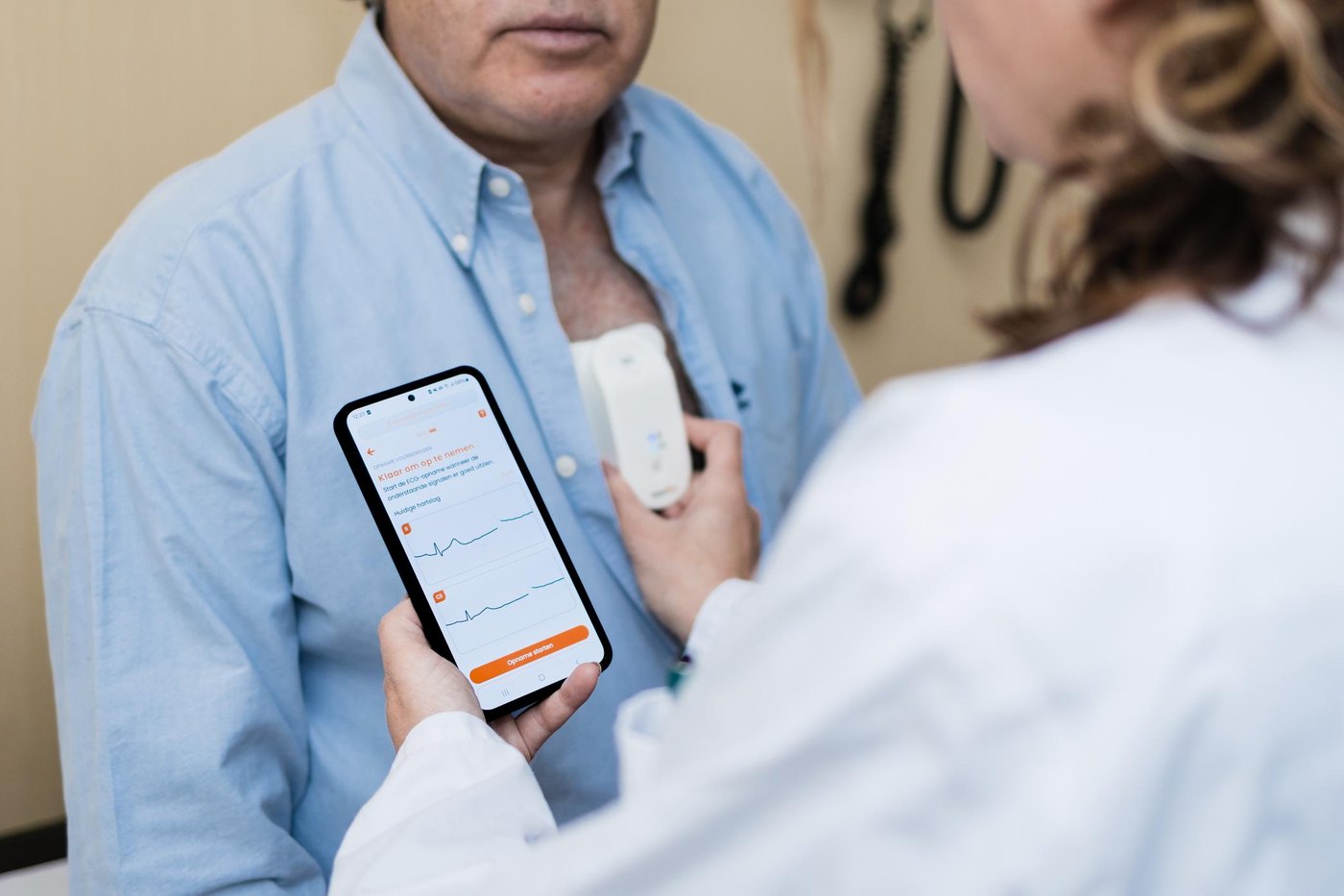 A clinician viewing a 12-lead ECG on a smartphone while a pocket-sized HeartEye ECG device rests on a patient&rsquo;s chest.