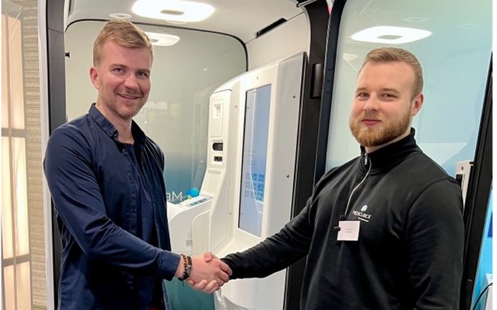 Cardiolyse and MedicubeX representatives shaking hands in front of a MedicubeX eHealth Station.