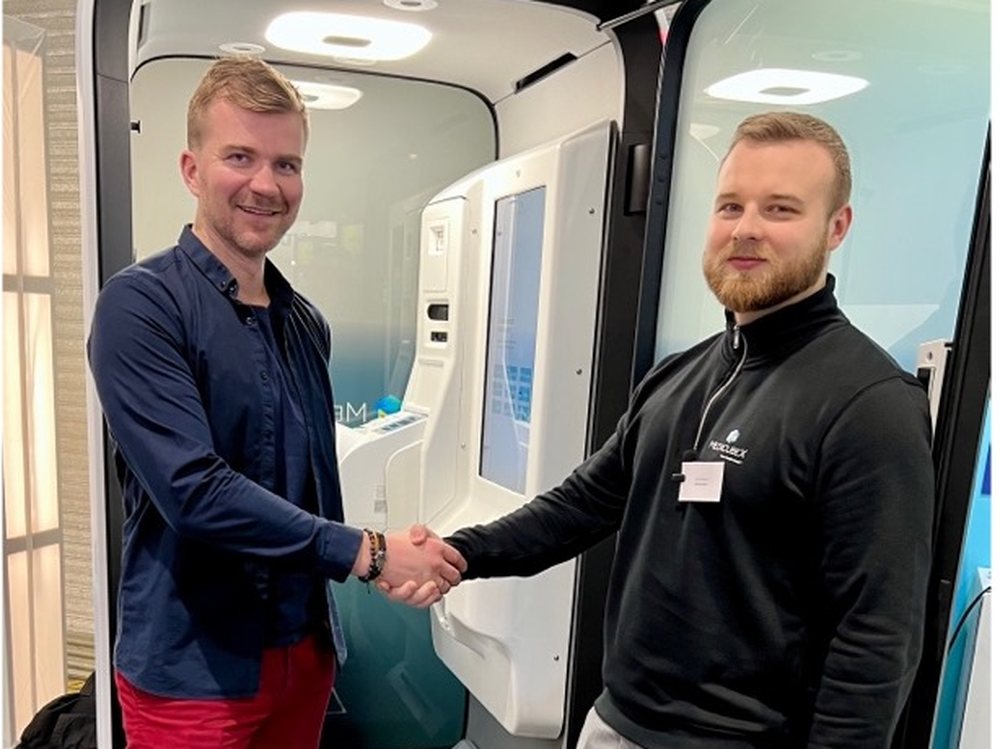 Cardiolyse and MedicubeX representatives shaking hands in front of a MedicubeX eHealth Station.